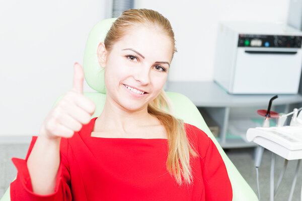 Happy female patient at dentist showing thumb-up