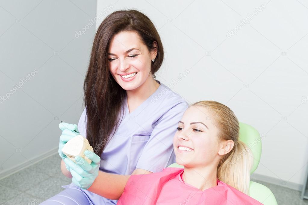 Dentist woman and female patient looking at dental implant examp