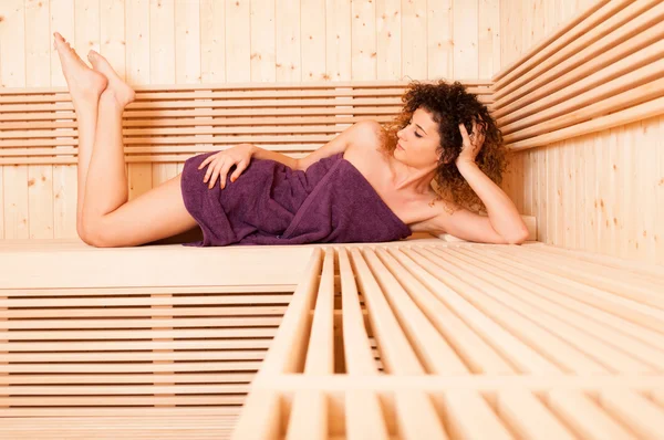 Jovem mulher encaracolada deitada no banco de madeira com os pés para cima — Fotografia de Stock