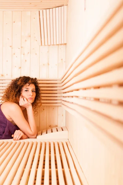 Curly feminino sentado relaxado no banco de madeira na sauna — Fotografia de Stock