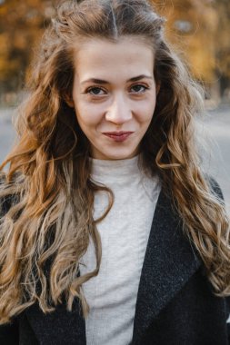 Güzel kıvırcık kız siyah paltolu sokakta duruyor.