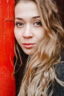 Güzel kıvırcık kız kırmızı kapının yanında duruyor. Siyah ceketli.