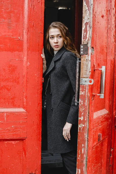 Όμορφη Σγουρή Κοπέλα Στέκεται Κοντά Στην Κόκκινη Πόρτα Μαύρο Παλτό — Φωτογραφία Αρχείου