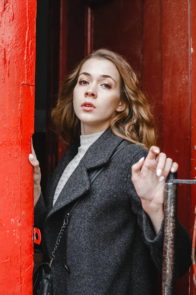 Gyönyörű Göndör Lány Áll Piros Ajtó Mellett Fekete Kabátban — Stock Fotó