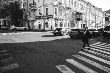 Siyah paltolu kıvırcık saçlı kız caddeden karşıya geçiyor.