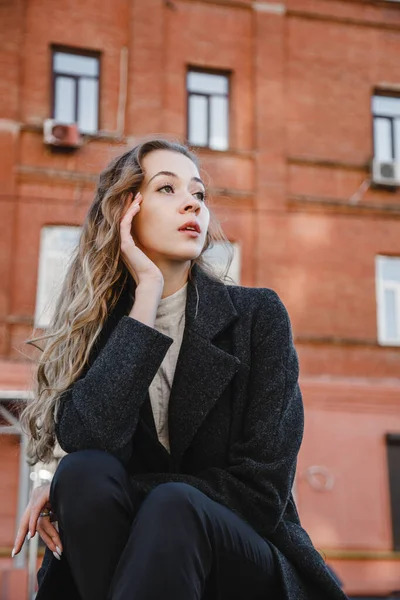 Kudrnatá Dívka Černém Kabátě Pózuje Pozadí Červené Budovy — Stock fotografie