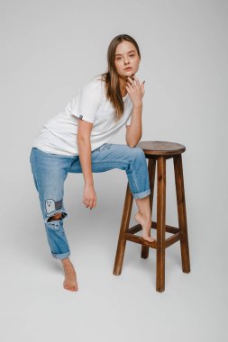 Model testleri. Uzun saçlı güzel bir kız sandalyeye yakın duruyor ve poz veriyor.