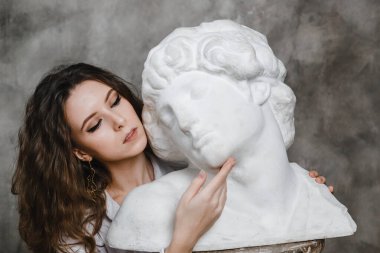 Güzel kıvırcık kız oturmuş, sıva heykeliyle sarılıyor.