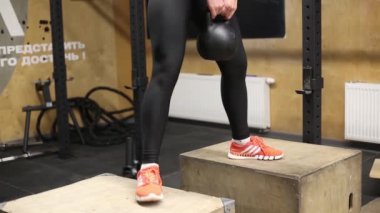 Sportif kızıl saçlı kız ahşap bloklarda kettlebell ile çömeliyor.