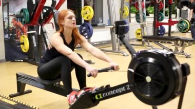 Sportif kızıl saçlı kız kürek çekme makinesiyle meşgul.