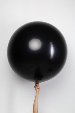 Kadın eli beyaz arka planda şişirilmiş bir siyah mat topu tutuyor. Sevgililer günü hediyesi.