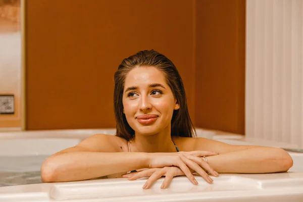 按摩后 黑发女人在按摩浴缸里放松下来 双手微笑着侧身 看着相机 — 图库照片