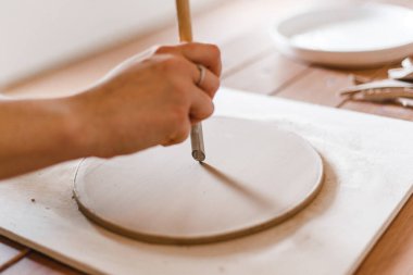 Kadın elleri çömlekçide masanın üzerinde merdaneyle killeri yuvarlıyor.