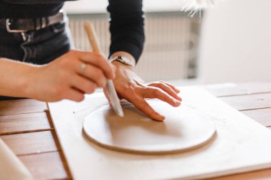 Kadın elleri çömlekçide masanın üzerinde merdaneyle killeri yuvarlıyor.