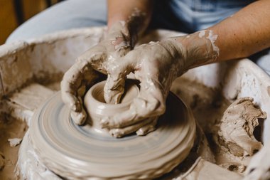 Kadın elleri kilden bir kupa yontuyor.