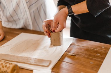 Kadın elleri çömlekçide masanın üzerinde merdaneyle killeri yuvarlıyor.