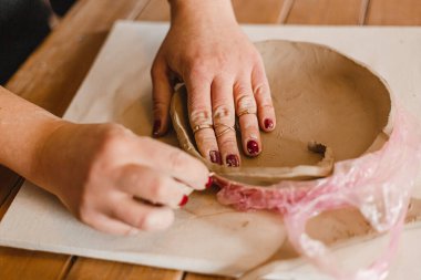 Kadın elleri çömlekçide masanın üzerinde merdaneyle killeri yuvarlıyor.
