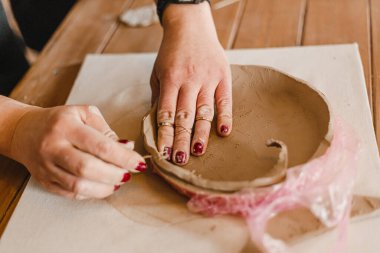 Kadın elleri çömlekçide masanın üzerinde merdaneyle killeri yuvarlıyor.