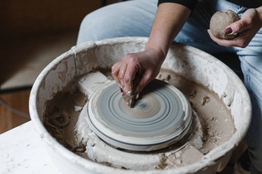 Kadın elleri çömlek atölyesindeki bir derste kilden güzel tabaklar yontuyor.