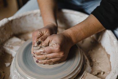 Kadın elleri çömlek atölyesindeki bir derste kilden güzel tabaklar yontuyor.