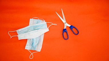 Koronavirüs ve makas koruyucu maskeler kırmızı arka planda yatar