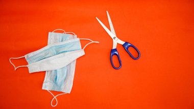 Koronavirüs ve makas koruyucu maskeler kırmızı arka planda yatar