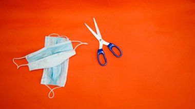 Koronavirüs ve makas koruyucu maskeler kırmızı arka planda yatar