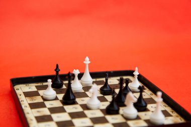 Kırmızı zemin üzerinde satranç taşları olan manyetik satranç tahtasıyla seyahat et. Satranç oyunu, beyaz ve siyah piyonlar.