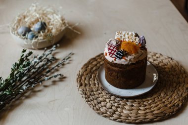 Bayram boyalı Paskalya bir tabakta, arka planda bir söğüt dalı ve boyalı yumurtalarla dolu bir sepet var.