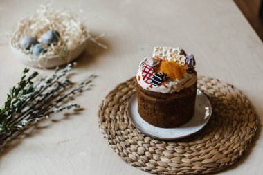 Bayram boyalı Paskalya bir tabakta, arka planda bir söğüt dalı ve boyalı yumurtalarla dolu bir sepet var.