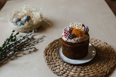 Bayram boyalı Paskalya bir tabakta, arka planda bir söğüt dalı ve boyalı yumurtalarla dolu bir sepet var.