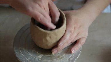 Kadın seramikçi elleri mumlarla kil tabakları yontuyor.
