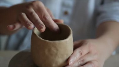 Kadın seramikçi elleri mumlarla kil tabakları yontuyor.