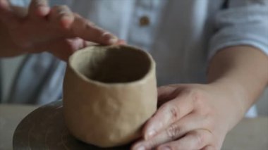 Kadın seramikçi elleri mumlarla kil tabakları yontuyor.