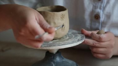 Kadın seramikçi elleri mumlarla kil tabakları yontuyor.