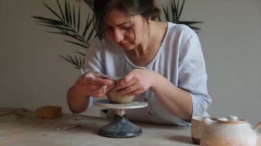 Kadın seramikçi elleri mumlarla kil tabakları yontuyor.
