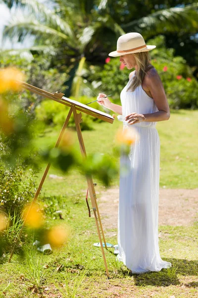 Karcsú festő nő fehér ruhában és kalapban, trópusi környezetben — Stock Fotó