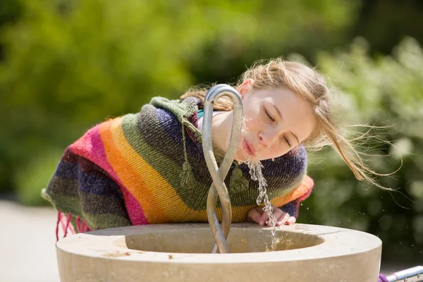 Blonde jeune fille boit à la fontaine publique — Photo