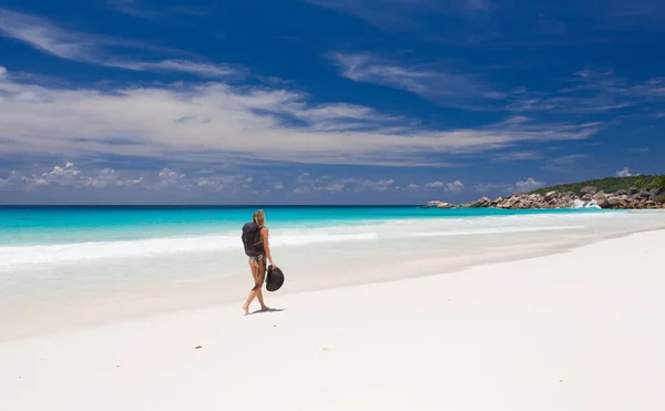 Blonde woman with backpack and hat, walks along a beach — Stock Photo, Image