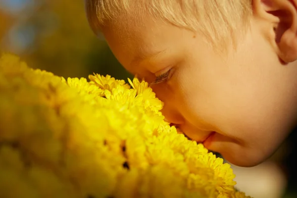 Ung pojke ansikte från sida, lukta gula blommor utomhus — Stockfoto