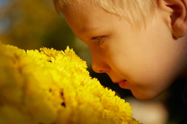 Jovem cara de menino de lado, cheirando flores amarelas ao ar livre — Fotografia de Stock