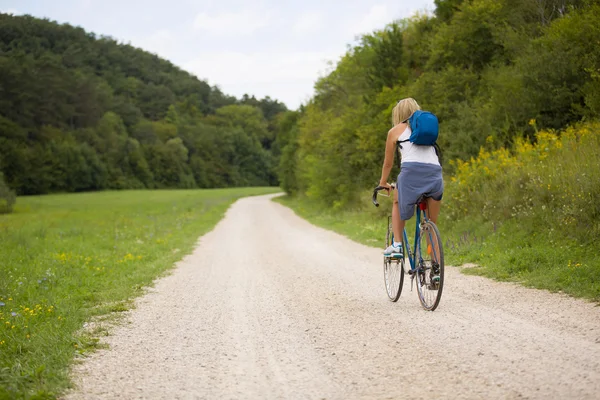 Блондинка їде на велосипеді на відкритому повітрі, поруч з лісом — стокове фото
