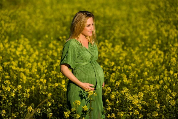 美丽而快乐的金发姑娘期待着穿着绿色衣服的妈妈 在一片黄色的花地中间微笑着 — 图库照片