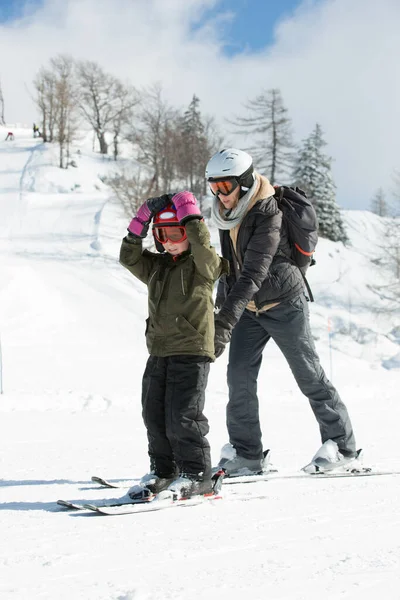 어미와 아들은 겨울에 눈덮인 산비탈에서 스키를 배운다 스톡 사진