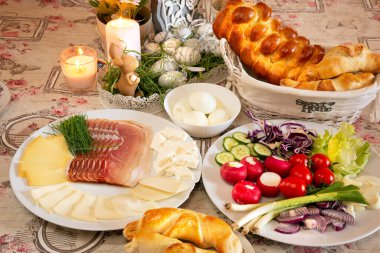 Paskalya kahvaltısı olan güzel bir mutfak ya da yemek masası. Peynir, yumurta, jambon, sebze, fırında yemek, güzel çiçek desenli tabaklar ve süsler..