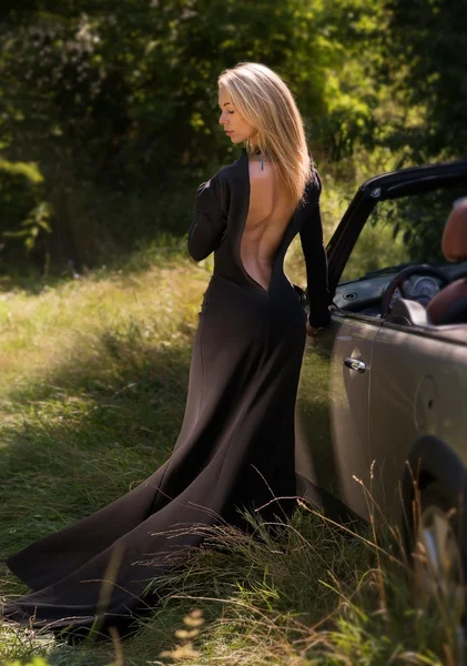 Σέξι, κομψή ξανθιά γυναίκα στο μαύρο μακρύ φόρεμα, εξωτερική, με cabrio αυτοκίνητο — Φωτογραφία Αρχείου