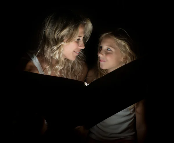 Une belle mère blonde et son enfant avec un grand livre dans l'obscurité . — Photo