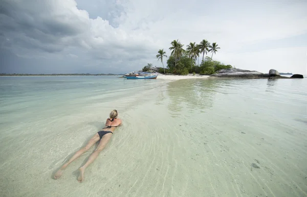 Mulher loira deita-se na água do oceano, perto de uma pequena ilha e barco — Fotografia de Stock