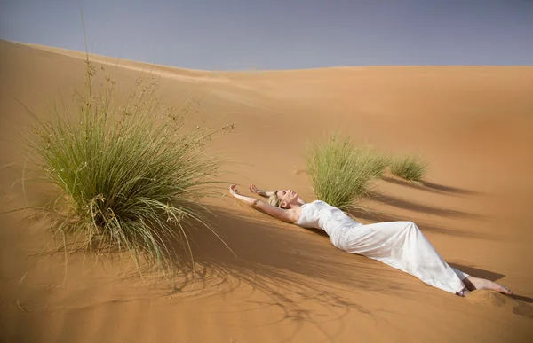 Mooie sexy vrouw legt in whte jurk tussen tuffets in zand woestijn — Stockfoto