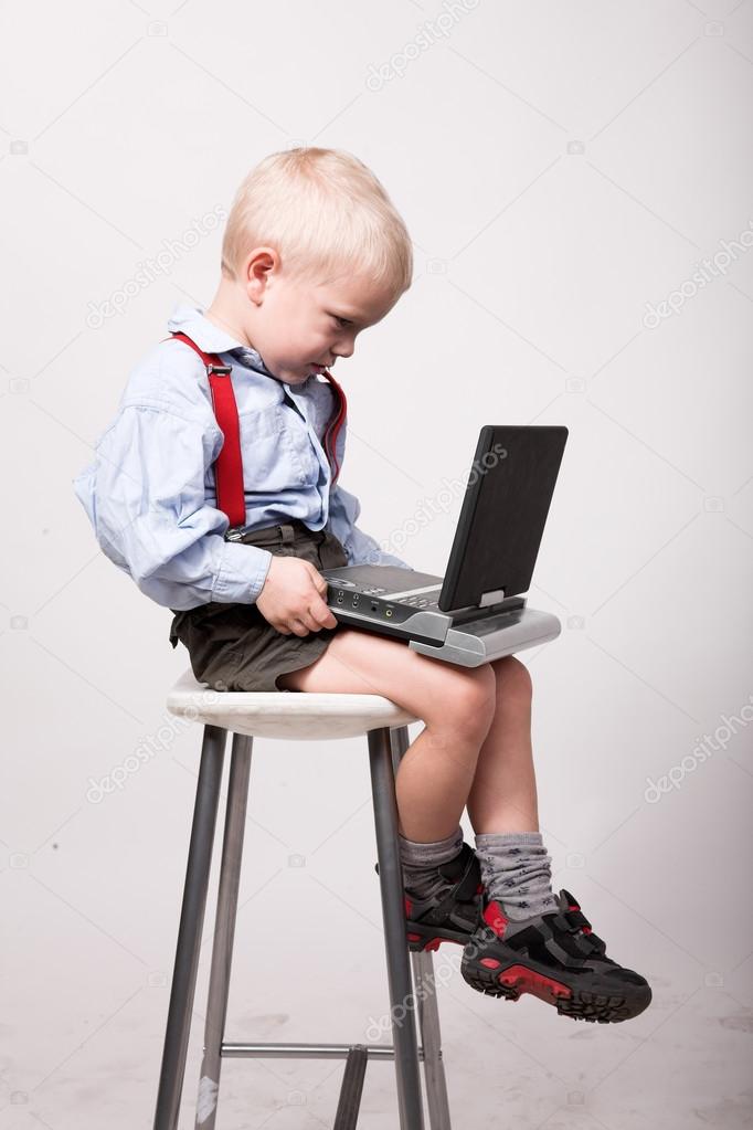 Little blonde boy sits on chair with portable dvd player